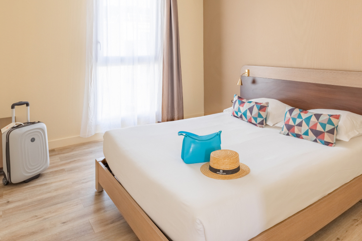 A comfortable room from the classic range at Appart'City with a king-size bed, geometric pillows, a suitcase next to the bed and a window that lets in natural light, creating a welcoming atmosphere for travellers.
