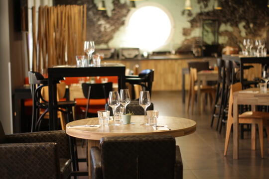 Intérieur accueillant du Restaurant Bistrot City Aéroport Le Bourget avec des tables rondes dressées, des chaises en tissu à motif, un éclairage doux et une décoration murale rustique, créant une ambiance chaleureuse et détendue.